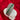 A silver-toned leaf-shaped cuff bracelet embellished with clear stones and a central row of green gemstones, displayed on a small white round stand against a red velvet background.