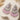 A pair of ornate dangling earrings displayed on a cream-colored sculptural stand. The earrings feature silver-toned metalwork adorned with clear rhinestones and pink faceted beads in a tiered design.